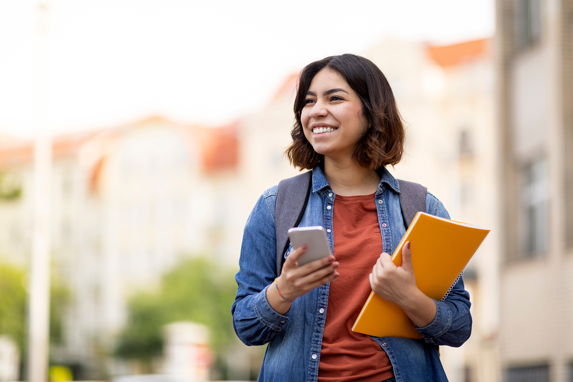female community college student smiling and walking with phone and notebook